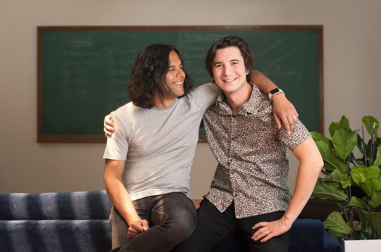 Robinhood co-founders Baiju Bhatt and Vladimir Tenev sitting together on a couch in front of a chalkboard.